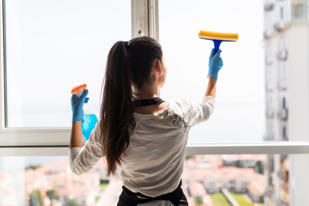 Happy professional cleaner washing window at home