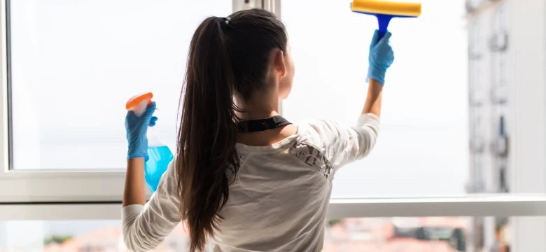 Happy professional cleaner washing window at home